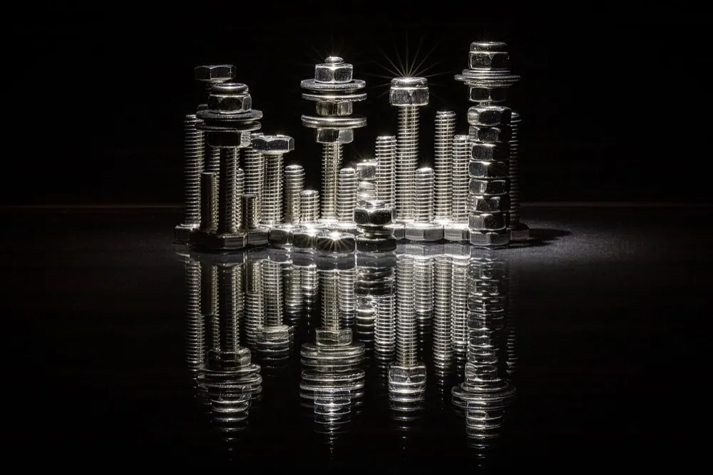 Hex bolts, nuts and washers stacked on a dark reflective surface